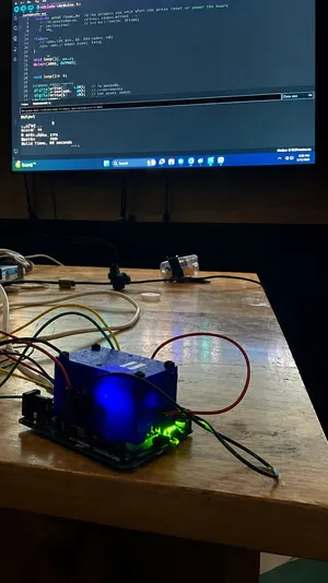 Assembled lead-detector electronics prototype mid-debug on a workbench, Arduino IDE visible on a monitor behind it